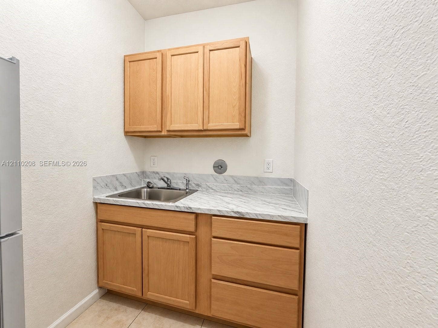 657 SE 30th Terrace, #A, Homestead, Homestead, FL 33033 Wood-finish cabinetry featuring upper and lower storage, stone-patterned laminate countertop, stainless steel drop-in sink with chrome faucet, and neutral tile flooring