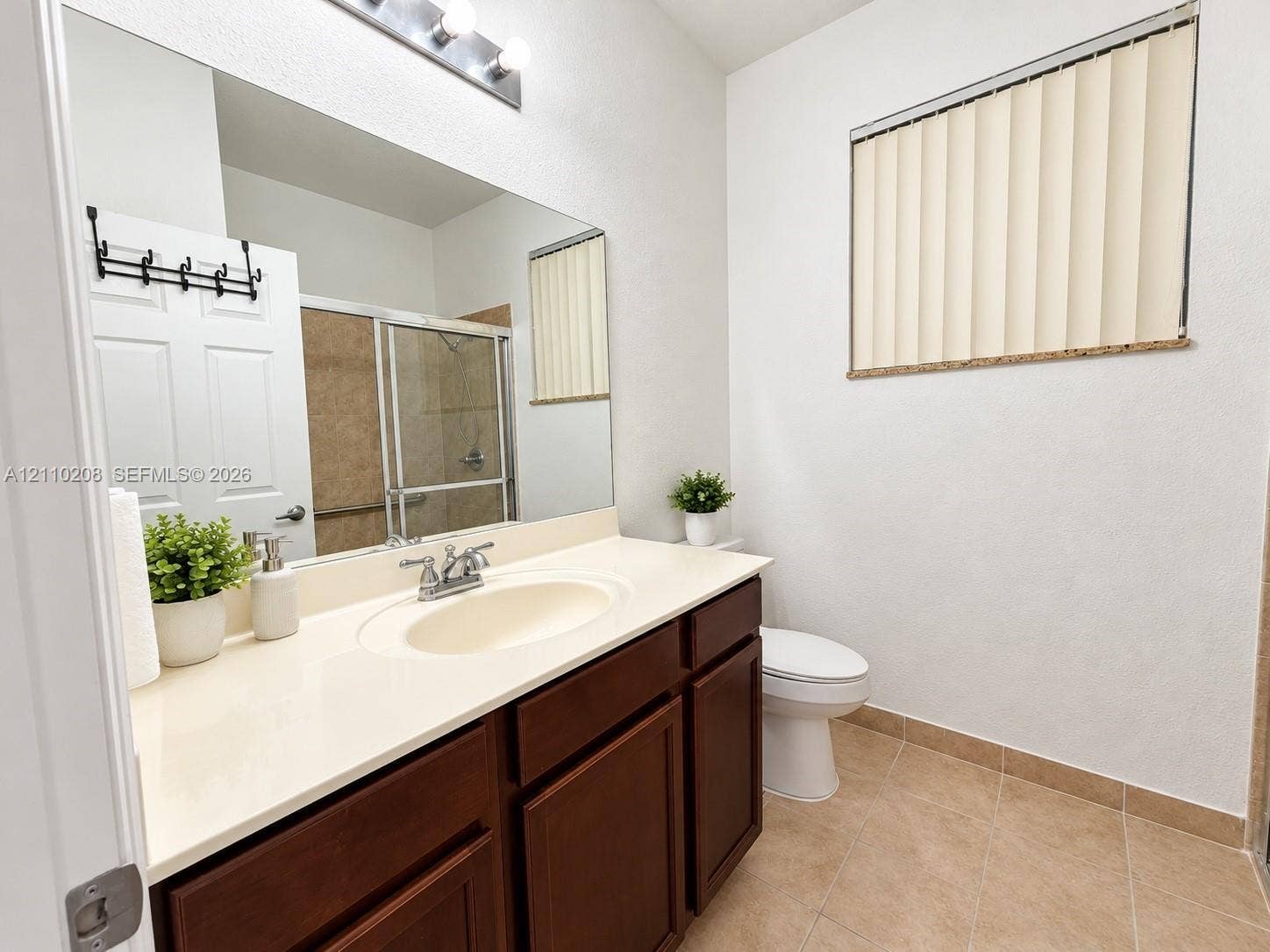 657 SE 30th Terrace, #A, Homestead, Homestead, FL 33033 Vanity featuring dark wood cabinetry, an integrated sink with chrome faucet, and a large wall-mounted mirror with multi-bulb overhead lighting, complemented by tile flooring and a sliding glass shower enclosure