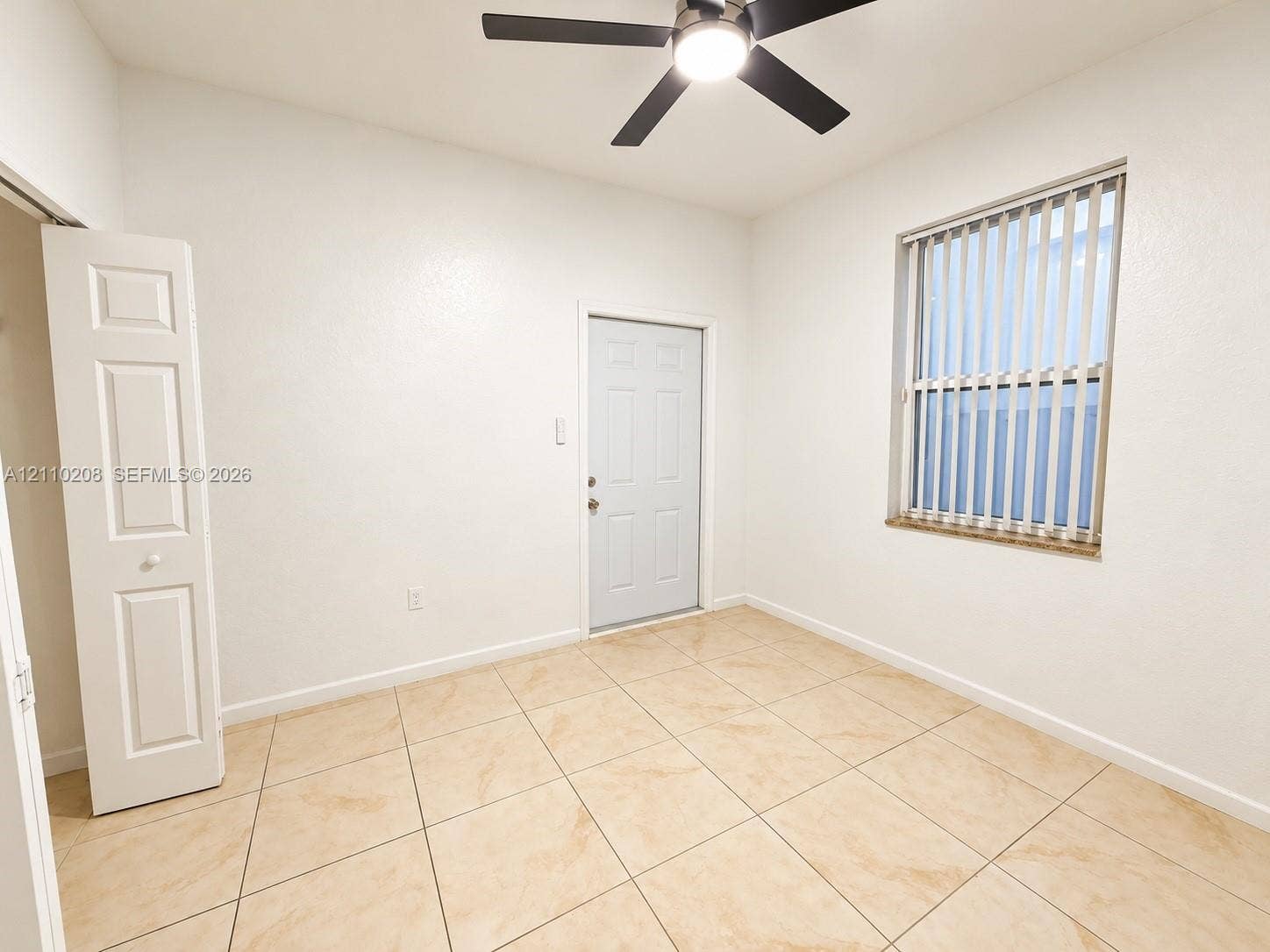 657 SE 30th Terrace, #A, Homestead, Homestead, FL 33033 Room featuring large-format neutral tile flooring, ceiling fan with integrated lighting, window with vertical blinds, and a built-in bifold closet