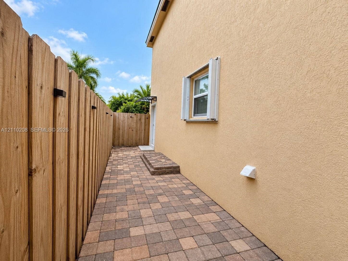 657 SE 30th Terrace, #A, Homestead, Homestead, FL 33033 Stucco exterior wall with a single-pane window featuring accordion shutters, multi-toned concrete paver walkway, and full-height wood-slat privacy fencing