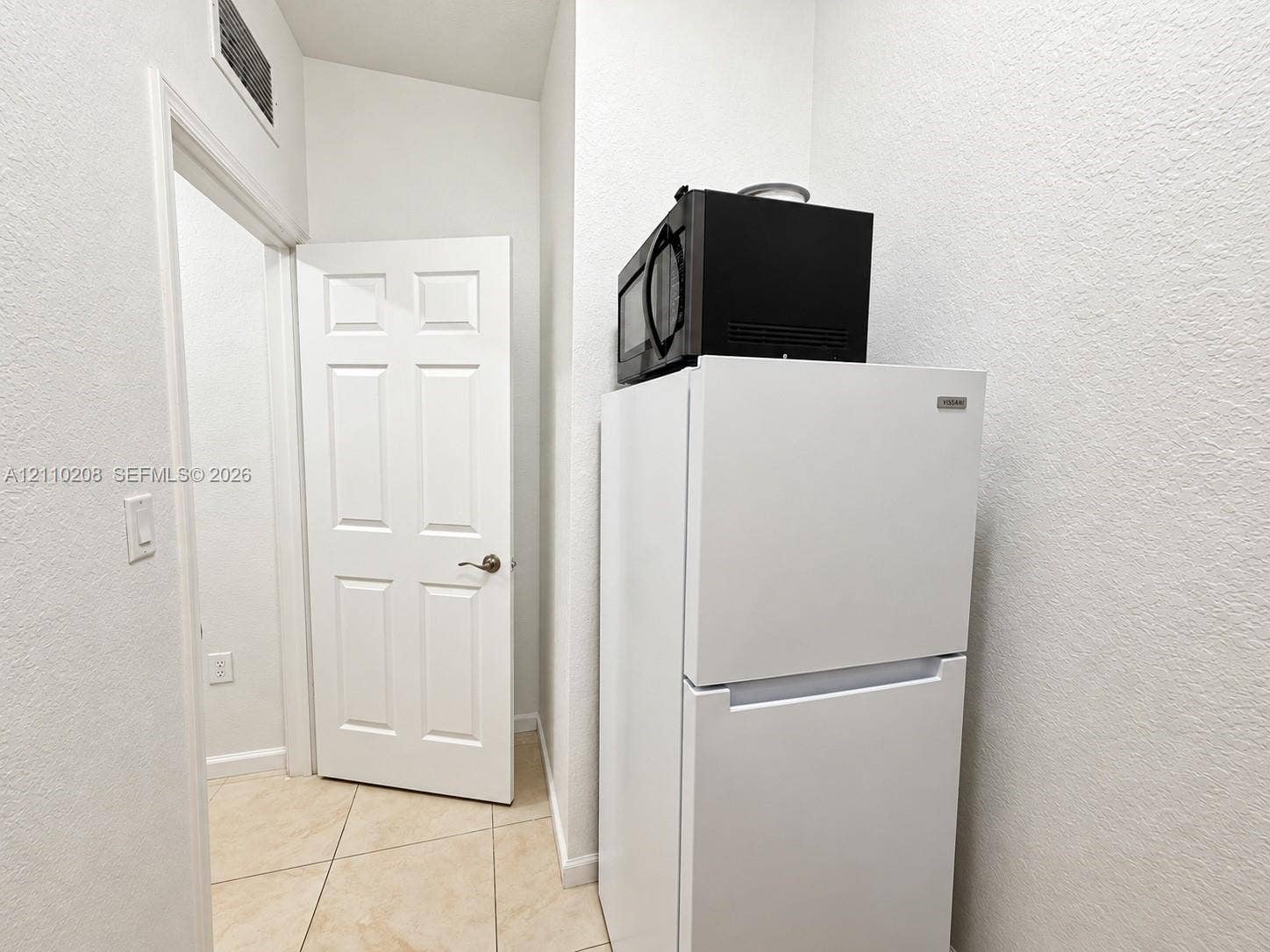 657 SE 30th Terrace, #A, Homestead, Homestead, FL 33033 Interior area featuring neutral tile flooring, a white six-panel door with a metallic handle, and smooth-finish walls