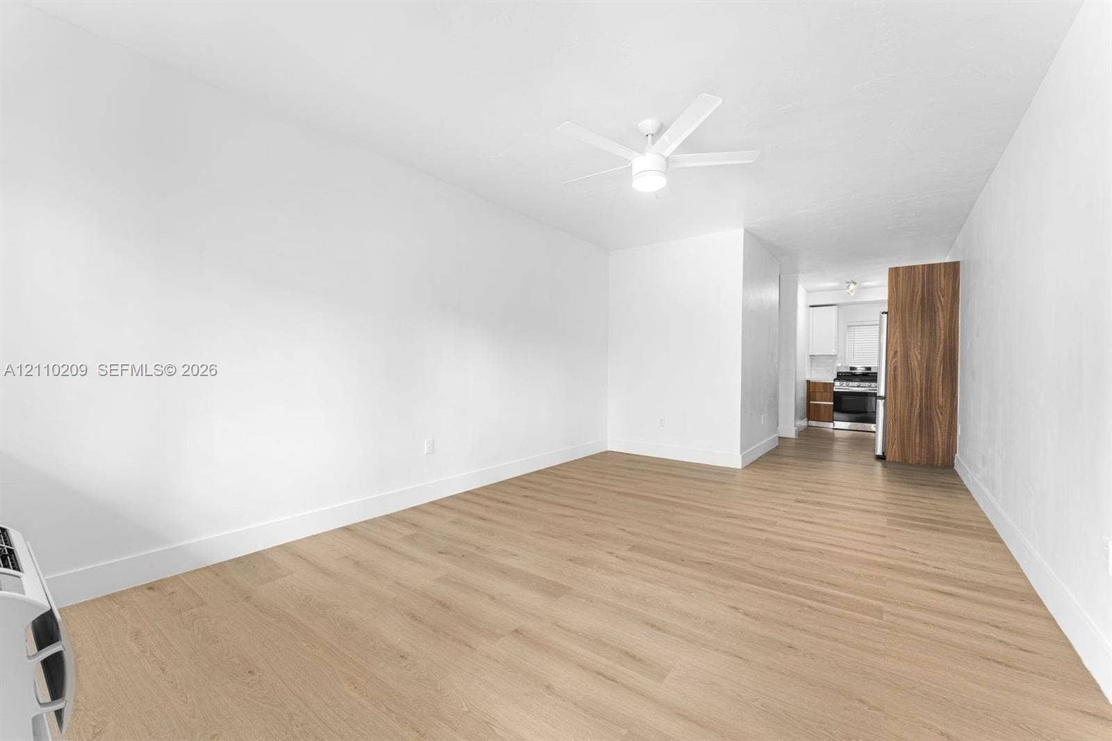 Interior space featuring wood-finish flooring, a neutral white color palette, and a ceiling-mounted light fixture with integrated fan