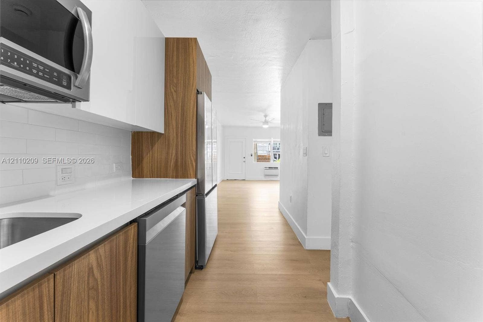 Kitchen featuring high-gloss white upper cabinetry, wood-finish lower cabinetry, solid-surface countertops, subway tile backsplash, and stainless steel appliances, complemented by wood-finish flooring