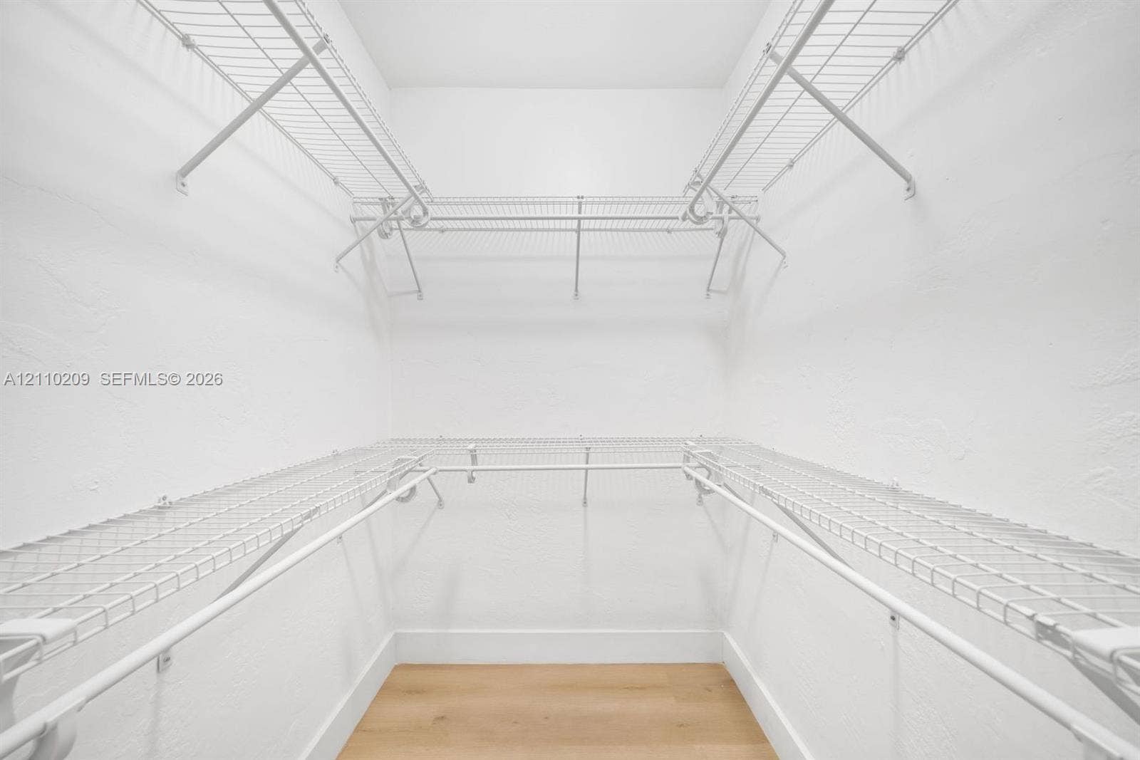 Walk-in closet featuring multi-level white wire shelving and wood-finish flooring