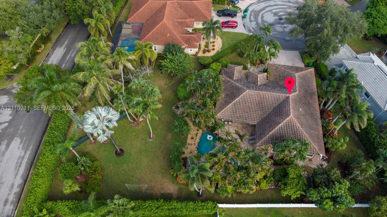 Aerial perspective of a property featuring a tile roof, an in-ground swimming pool, extensive landscaping with mature palm trees, and a perimeter fence