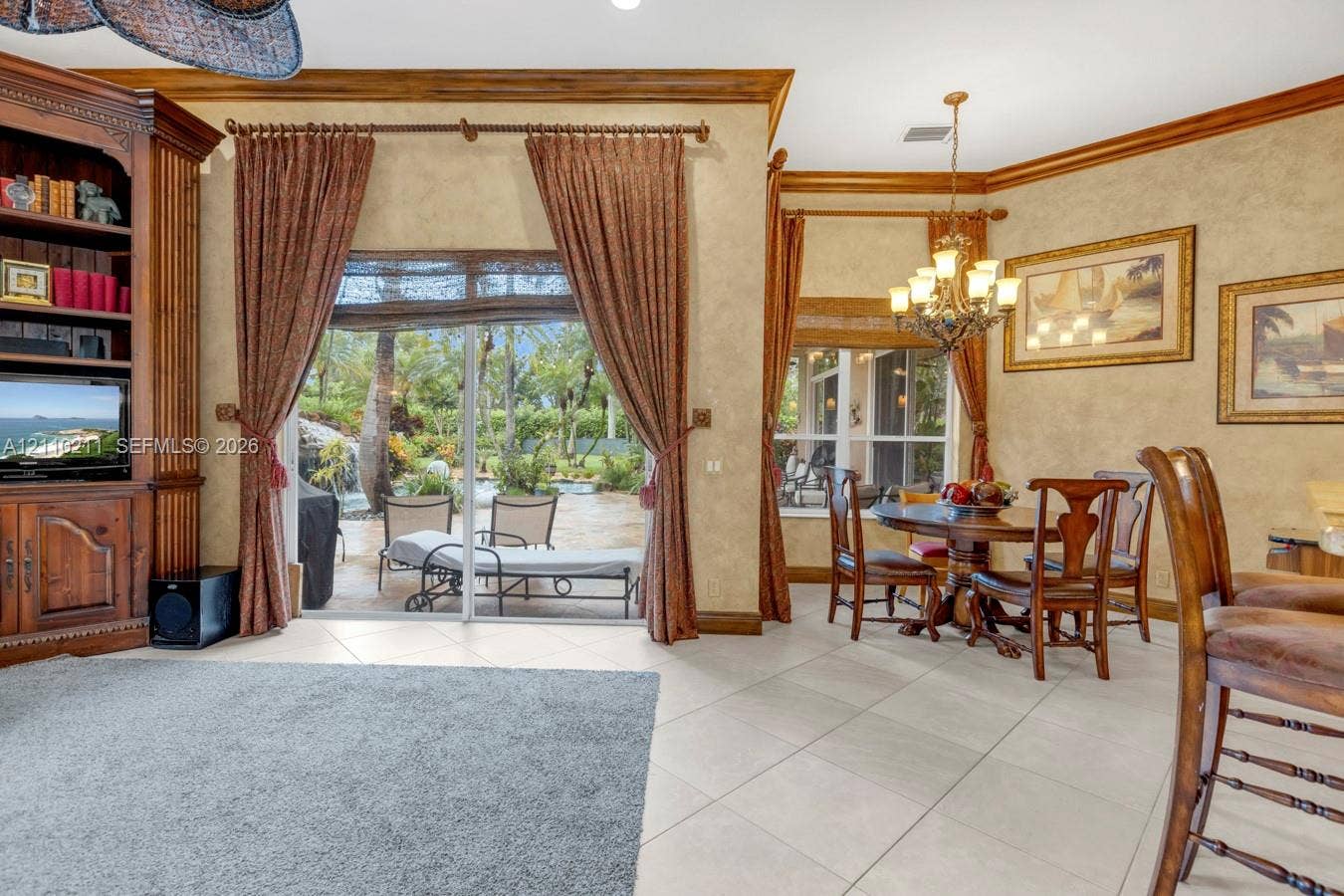 Living area featuring tile flooring, built-in floor-to-ceiling cabinetry, sliding glass doors with exterior access, crown molding, and a multi-light chandelier