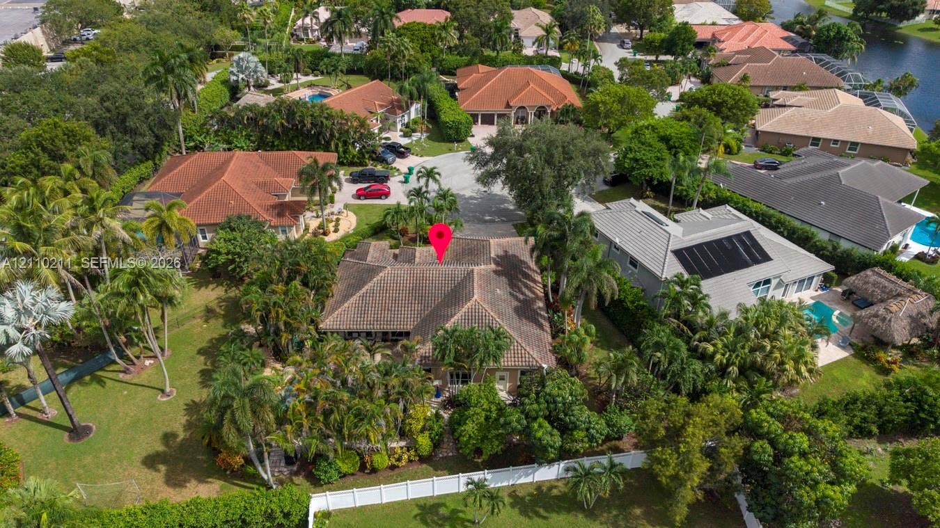 Aerial view of residence featuring a tile roof, multi-car driveway, lush mature landscaping, and white perimeter fencing