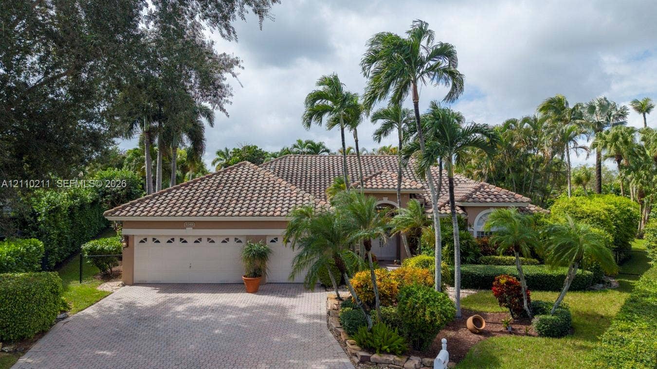 Single-story residence featuring a tile roof, paver driveway, multi-car garage, and mature landscaping