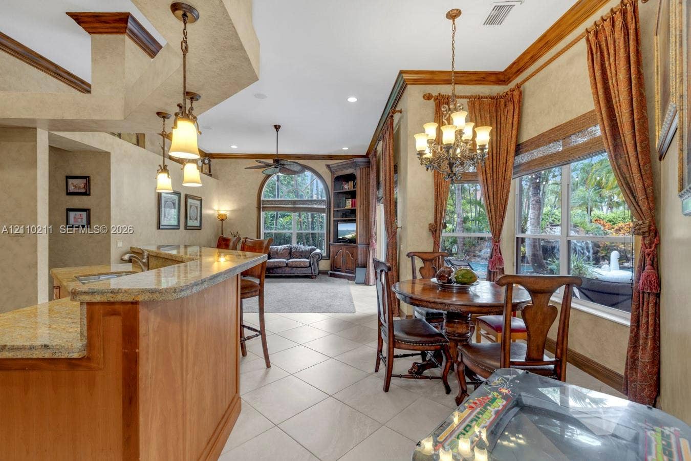Kitchen featuring stone-finish countertops, natural wood cabinetry, built-in corner shelving, ceramic tile flooring, and decorative multi-light chandeliers