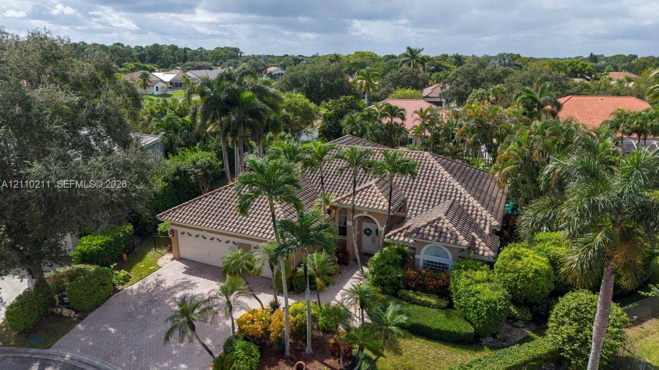 Single-story residence featuring a tile roof, paved driveway, two-car garage, and established landscaping with mature palm trees