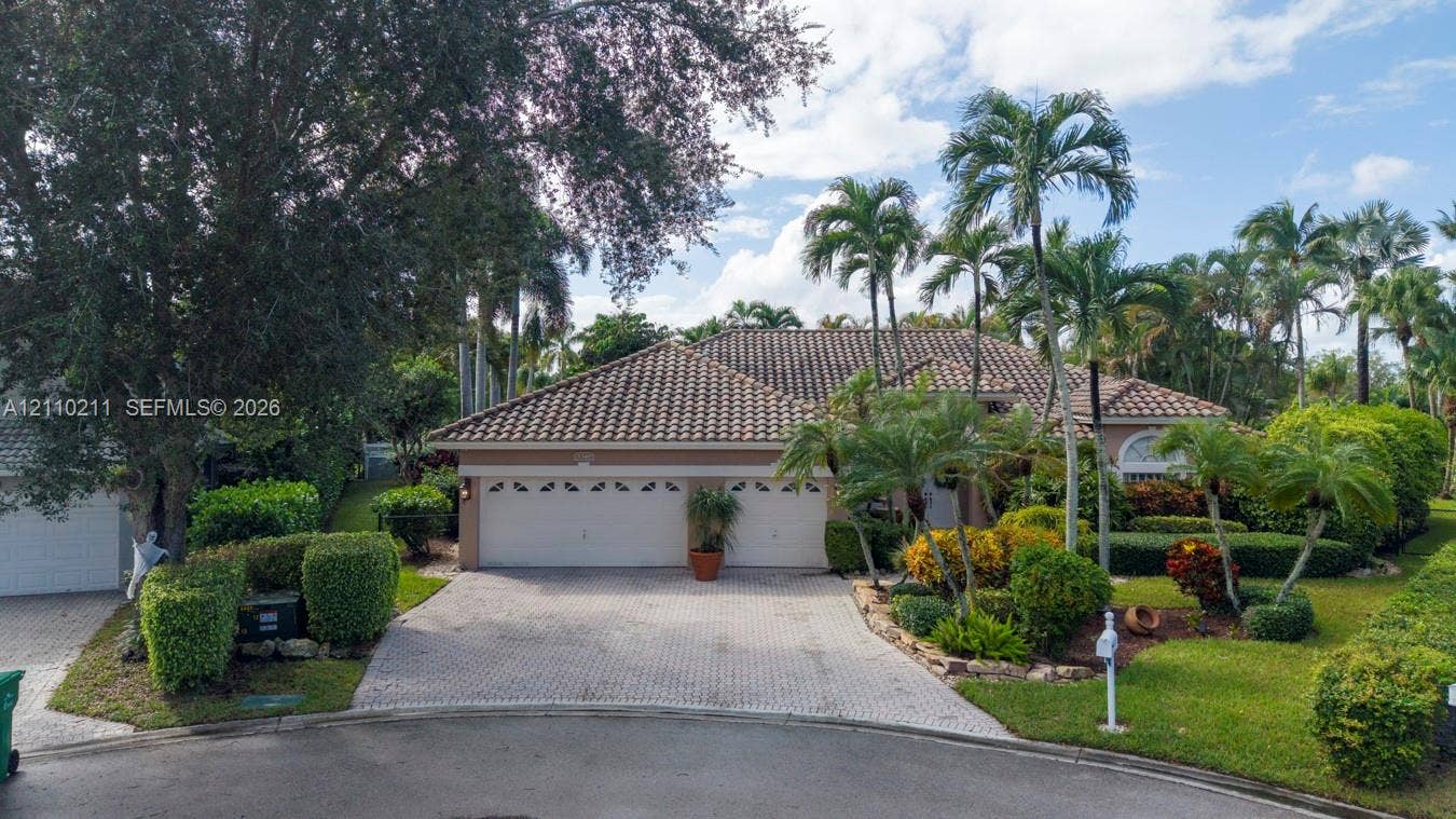Exterior featuring a tile roof, two-car garage, paver driveway, and mature tropical landscaping