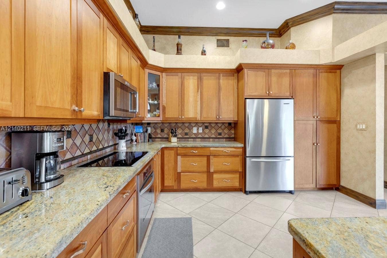 Kitchen featuring wood cabinetry, stone countertops, a tiled backsplash, stainless steel appliances, and tile flooring