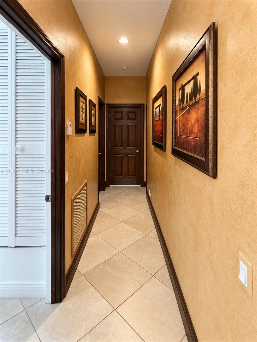 Hallway featuring neutral-toned textured wall finishes, tile flooring laid on a diagonal, recessed ceiling lighting, and solid wood-finish doors with matching trim