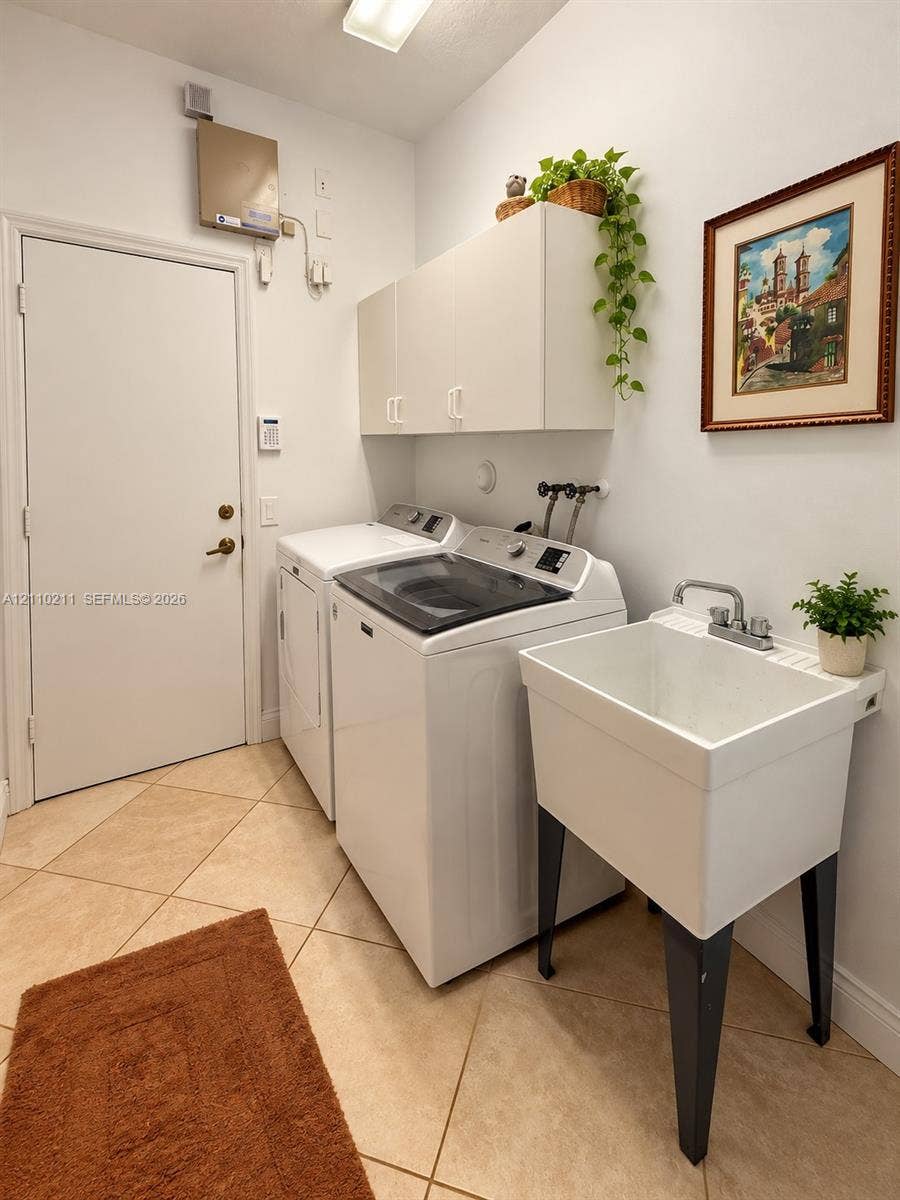 Laundry area featuring tile flooring, white built-in wall cabinetry, and a deep basin utility sink with a dual-handle faucet