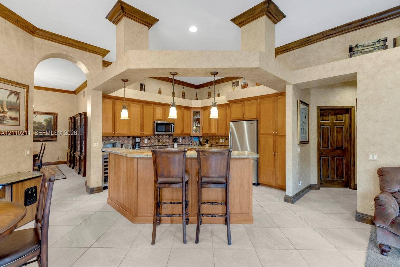 Kitchen featuring custom wood cabinetry, stone countertops, a multi-tiered peninsula island, tile flooring, and hanging pendant lighting