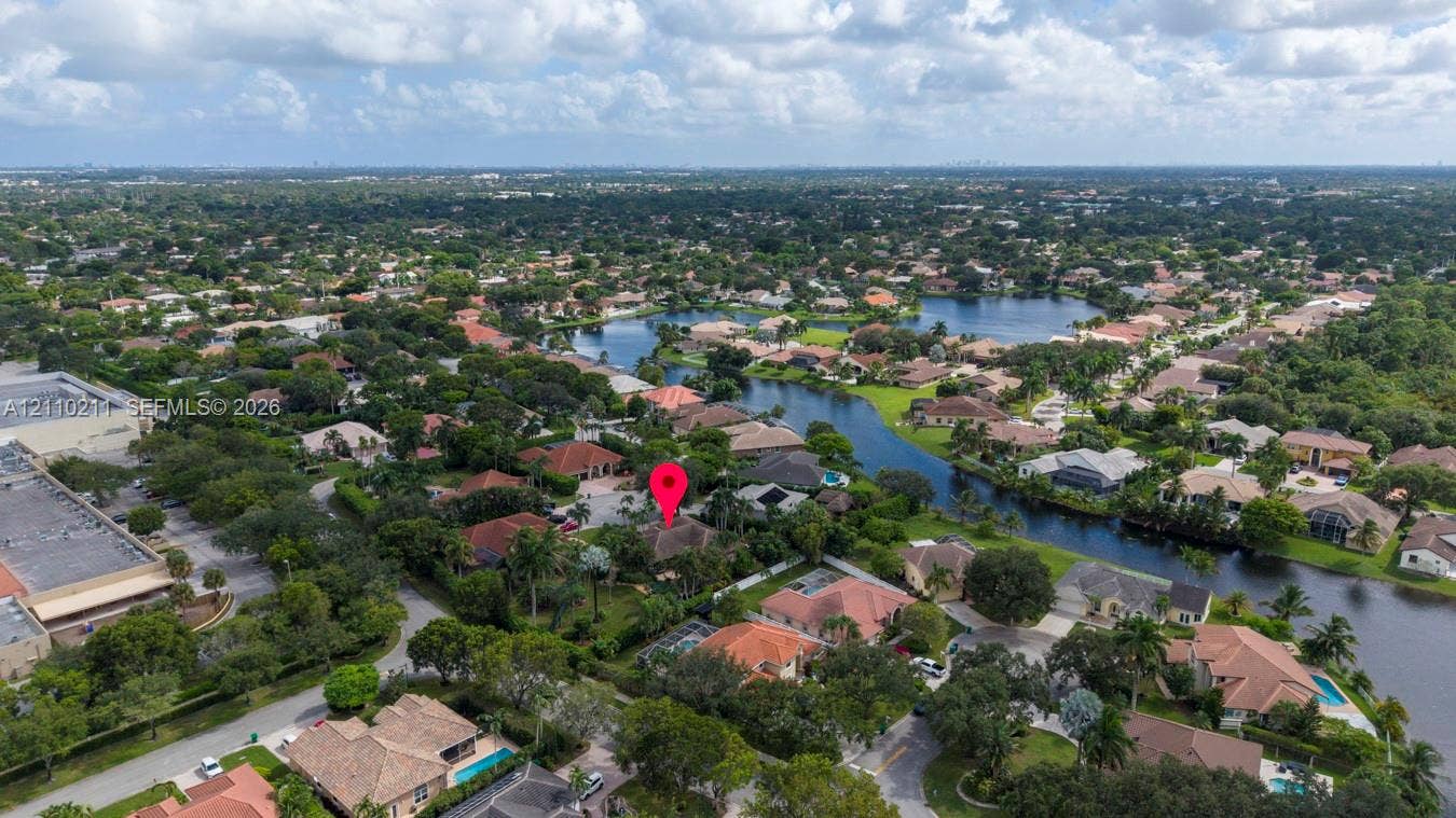 Aerial perspective of a residential property situated in a suburban community, featuring mature tropical landscaping and proximity to a winding waterway