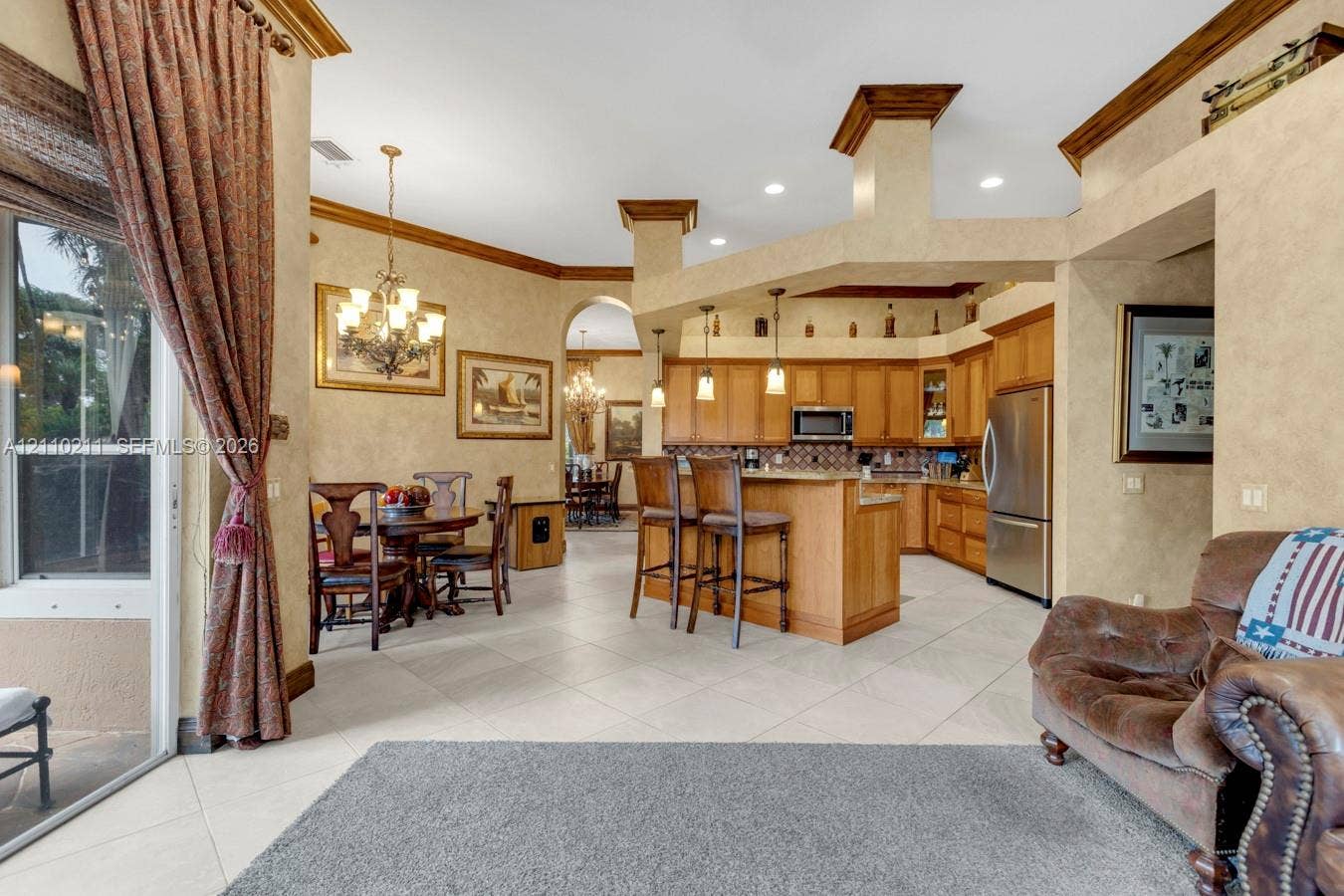 Open-concept kitchen featuring wood cabinetry, stainless steel appliances, a breakfast bar, recessed lighting, and tile flooring