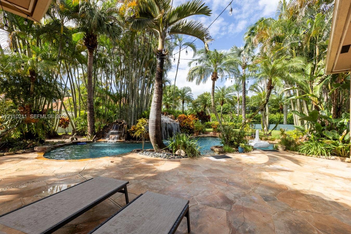 Outdoor area featuring flagstone hardscaping, custom swimming pool with integrated stone waterfall, and mature palm landscaping