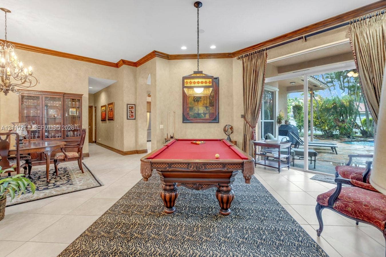 Spacious room featuring neutral tile flooring, crown molding, a decorative multi-light chandelier, a stained-glass style pendant fixture, and large sliding glass doors