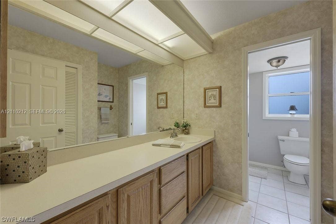 407 SW 37, Cape Coral, FL 33914 Full-width vanity featuring wood-finish cabinetry, solid surface countertop with integrated basin, expansive wall-to-wall mirror, and overhead soffit lighting