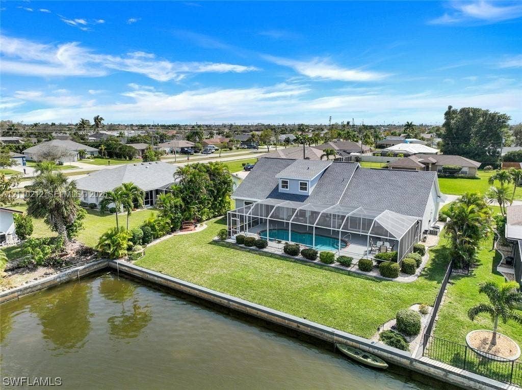 407 SW 37, Cape Coral, FL 33914 Waterfront property featuring a screened-in lanai with a swimming pool, concrete seawall, and landscaped lawn