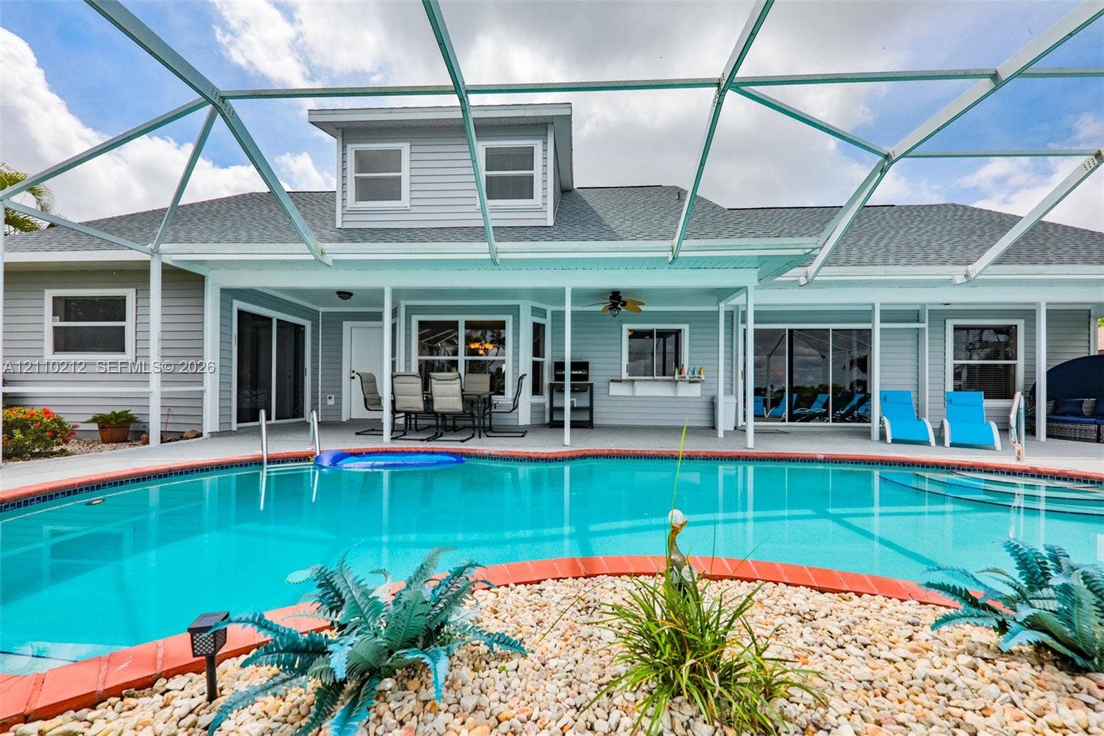 407 SW 37, Cape Coral, FL 33914 In-ground swimming pool with brick-style coping, enclosed by a screened lanai with a covered patio area featuring a built-in outdoor service counter and ceiling fan