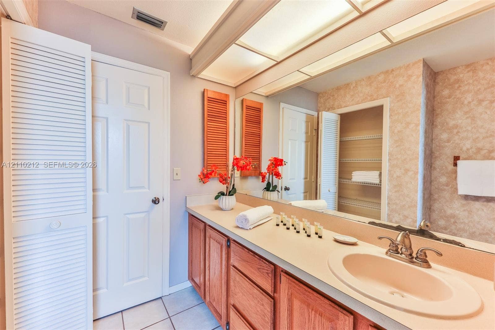 407 SW 37, Cape Coral, FL 33914 Bathroom vanity featuring wood cabinetry, a neutral countertop with an integrated basin, a full-width wall mirror, recessed overhead lighting, and built-in louvered-door cabinetry