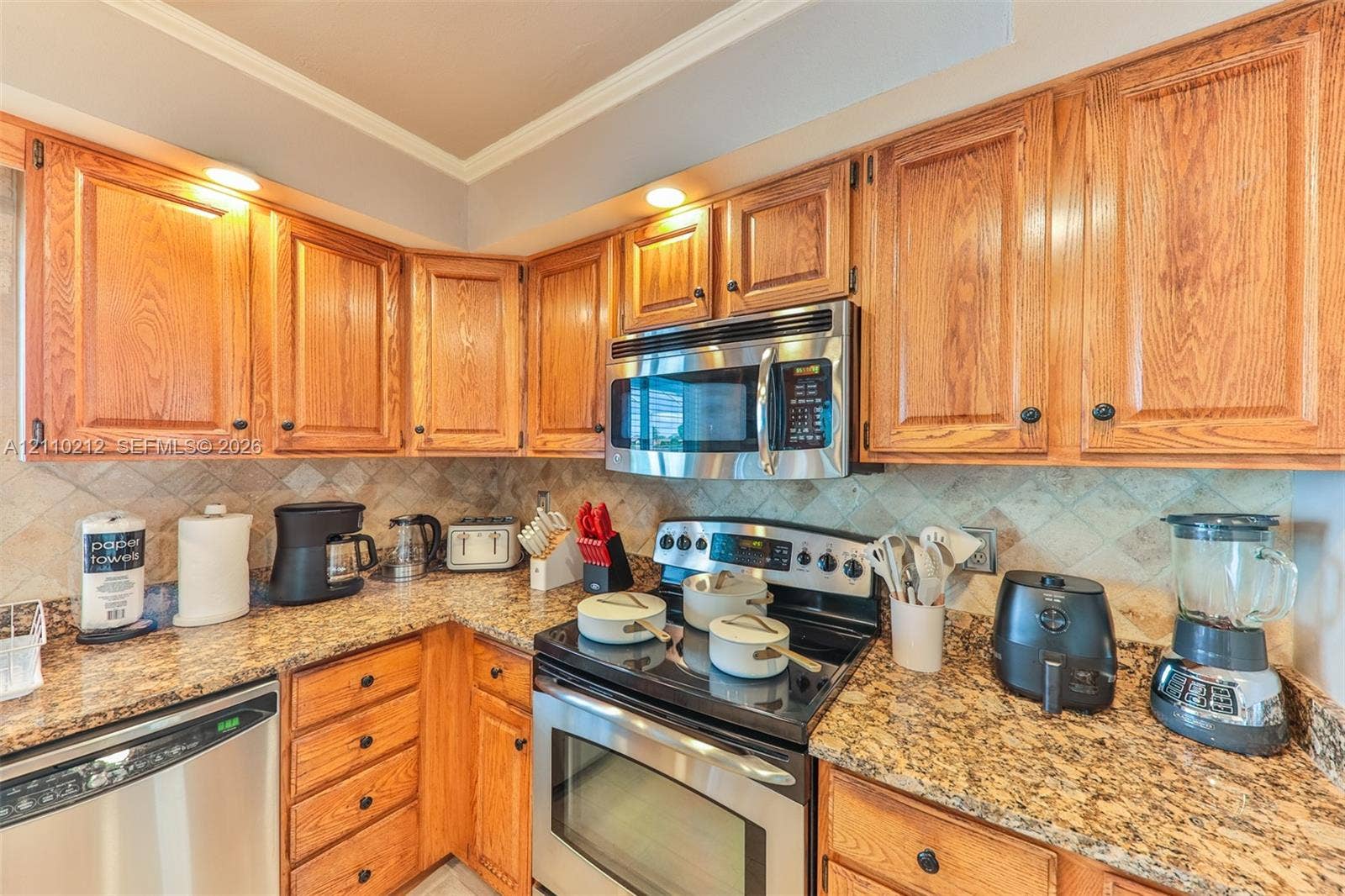 407 SW 37, Cape Coral, FL 33914 Kitchen featuring medium-tone wood cabinetry, stone-surface countertops, stone tile backsplash, and stainless steel appliances including a built-in microwave and range