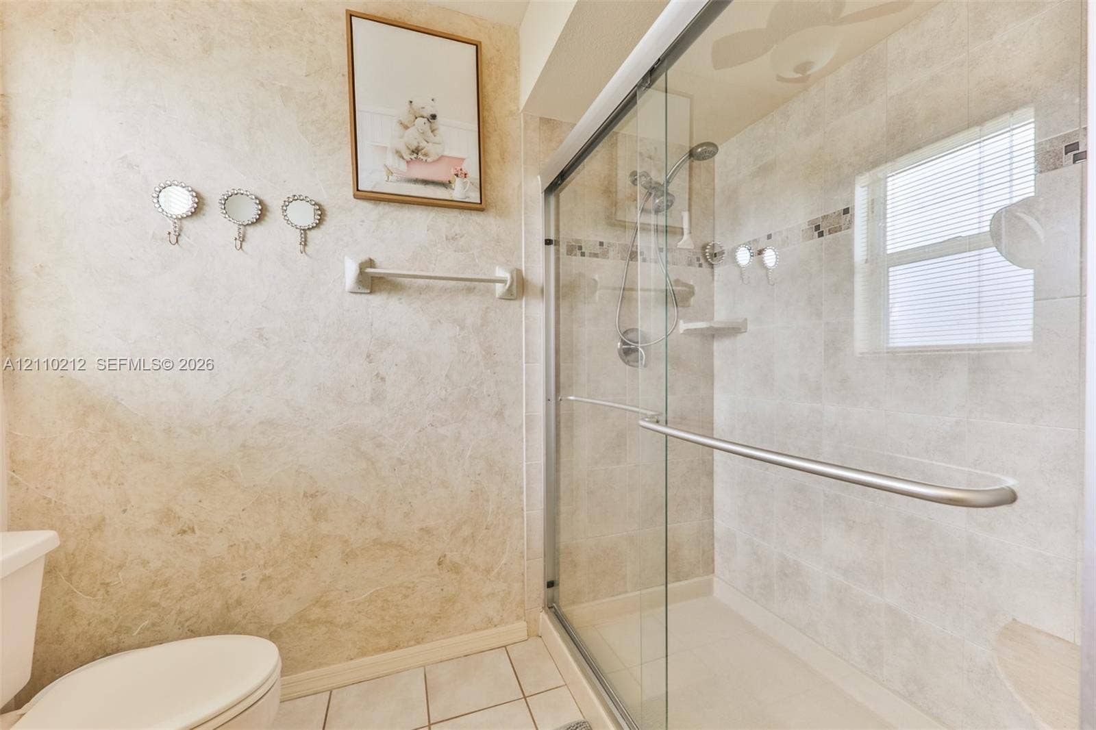 407 SW 37, Cape Coral, FL 33914 Walk-in shower enclosure with a sliding glass door, neutral-toned tiled walls, a built-in corner shelf, and a polished metal shower fixture