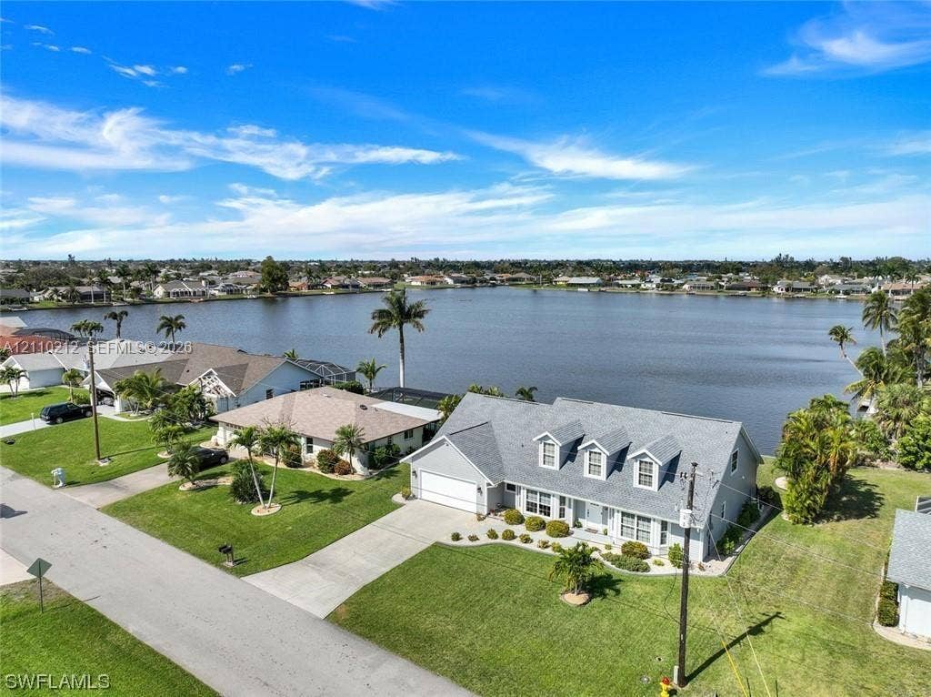 407 SW 37, Cape Coral, FL 33914 Waterfront property featuring a multi-gable roofline, attached two-car garage, concrete driveway, and expansive lawn area