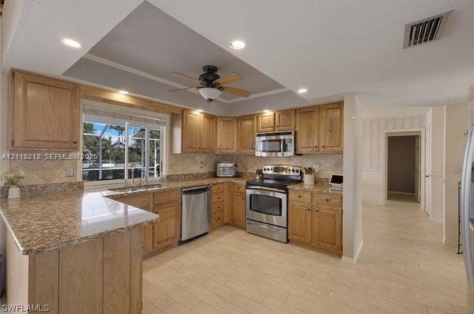 407 SW 37, Cape Coral, FL 33914 Kitchen featuring light wood cabinetry, stone-finish countertops, stainless steel appliances, a recessed tray ceiling, and tile flooring
