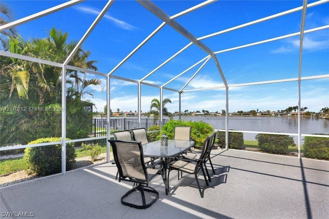 407 SW 37, Cape Coral, FL 33914 Screened-in lanai featuring a concrete deck and a metal frame enclosure, overlooking a lake with mature landscaping