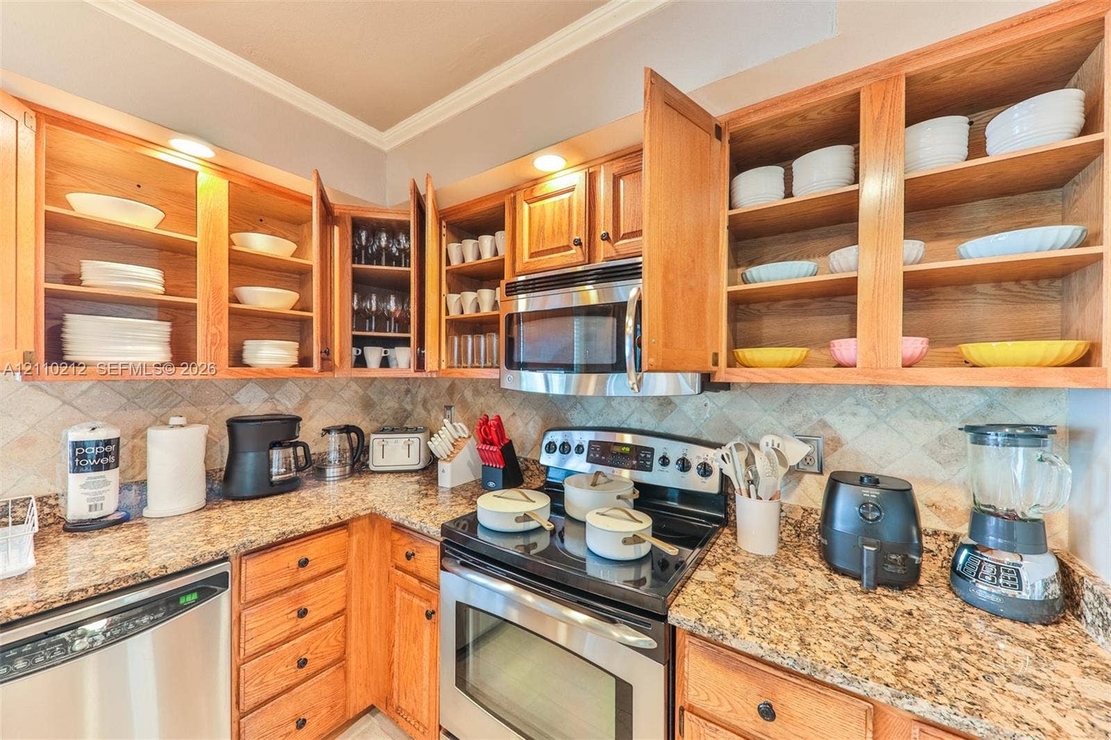 407 SW 37, Cape Coral, FL 33914 Kitchen featuring wood cabinetry, stone countertops, stone tile backsplash, stainless steel microwave, and stainless steel dishwasher