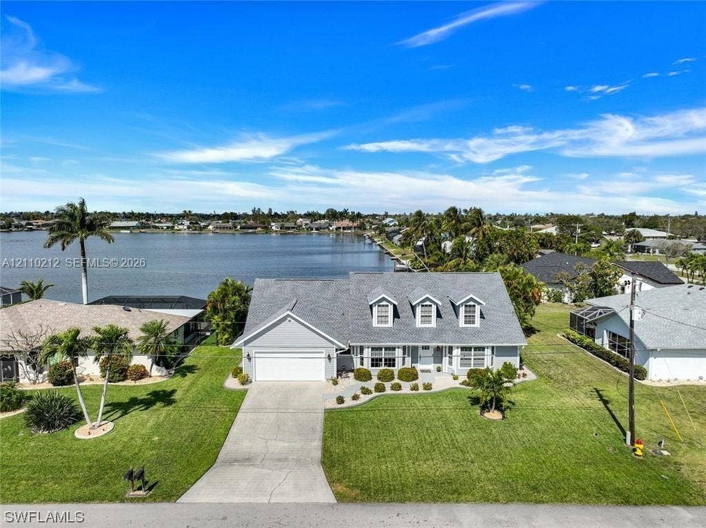 407 SW 37, Cape Coral, FL 33914 Waterfront residence featuring a shingle roof, three front-facing dormer windows, attached two-car garage, and expansive lawn