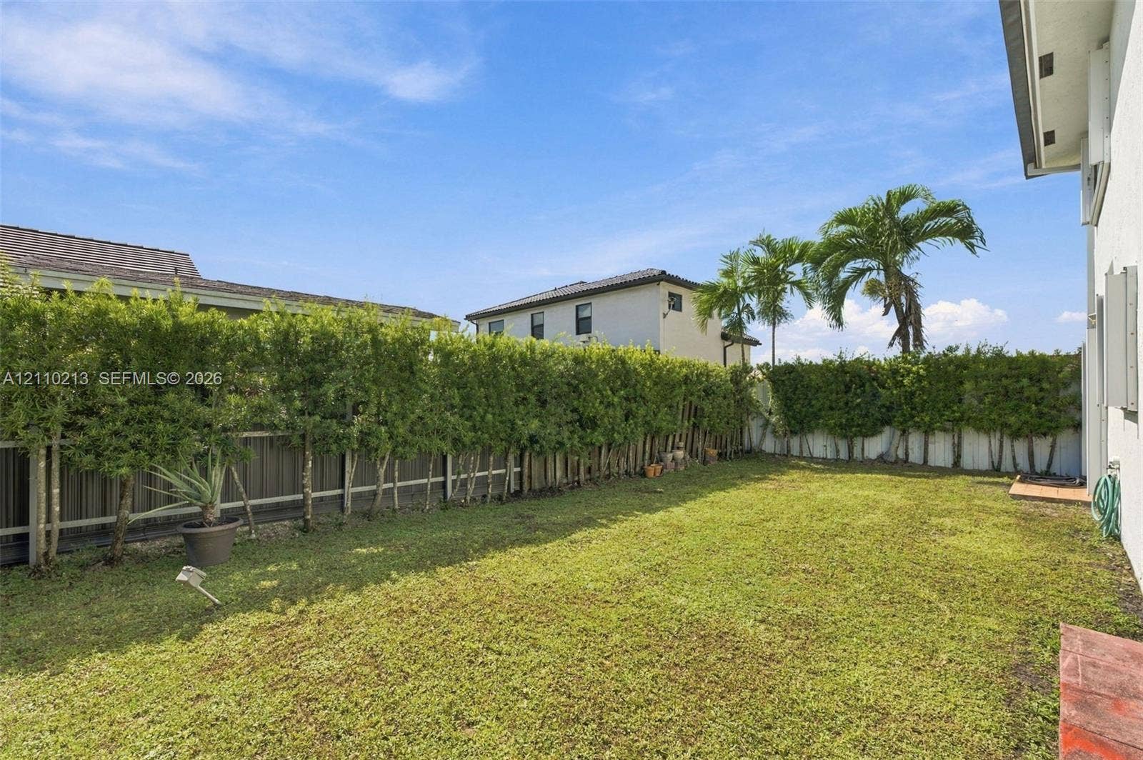 Private backyard featuring a grass lawn, perimeter hedges, and vertical fencing