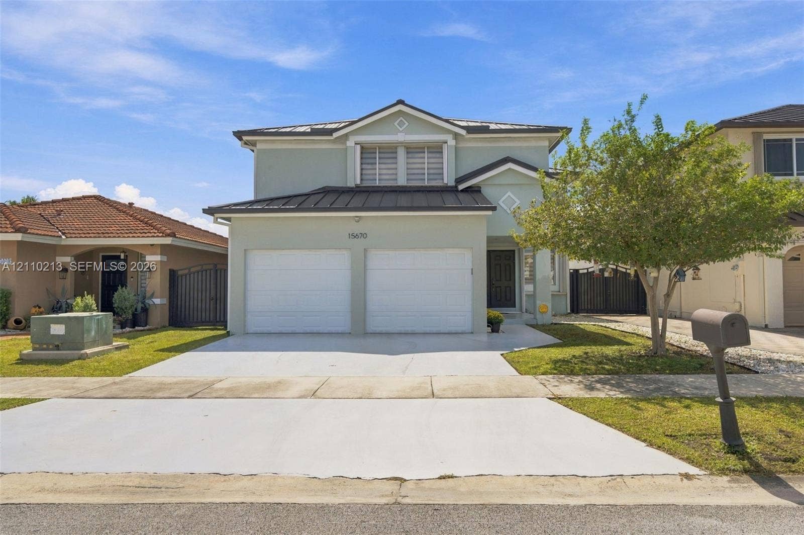 Two-story residence featuring a light-toned stucco exterior, a metal roof, an attached two-car garage, and a paved driveway