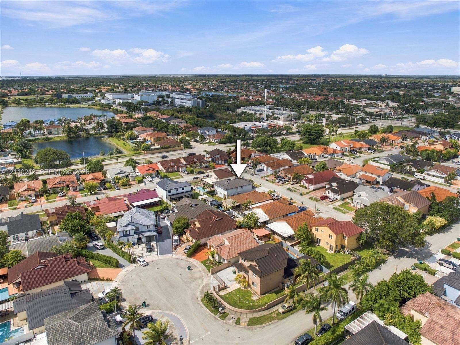 Aerial view of a residential property situated within a suburban neighborhood featuring a cul-de-sac street layout, nearby water features, and established greenery