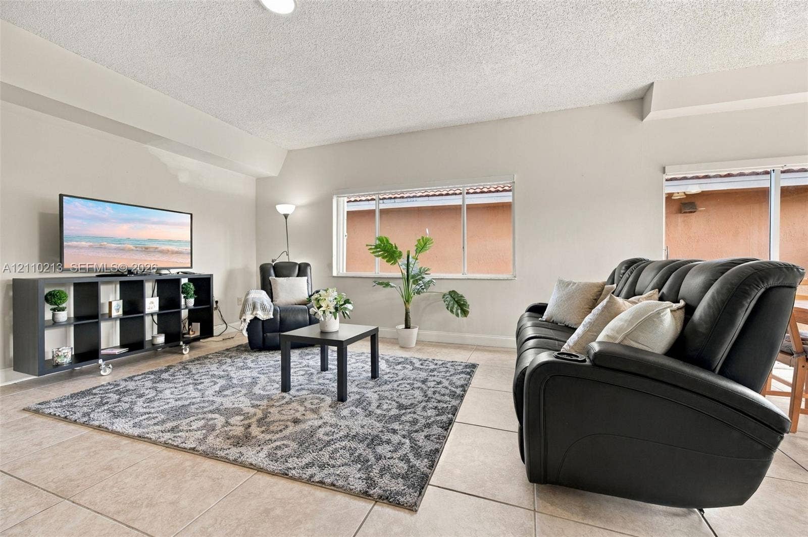 Neutral-toned interior space featuring ceramic tile flooring, expansive windows, and a sliding glass door