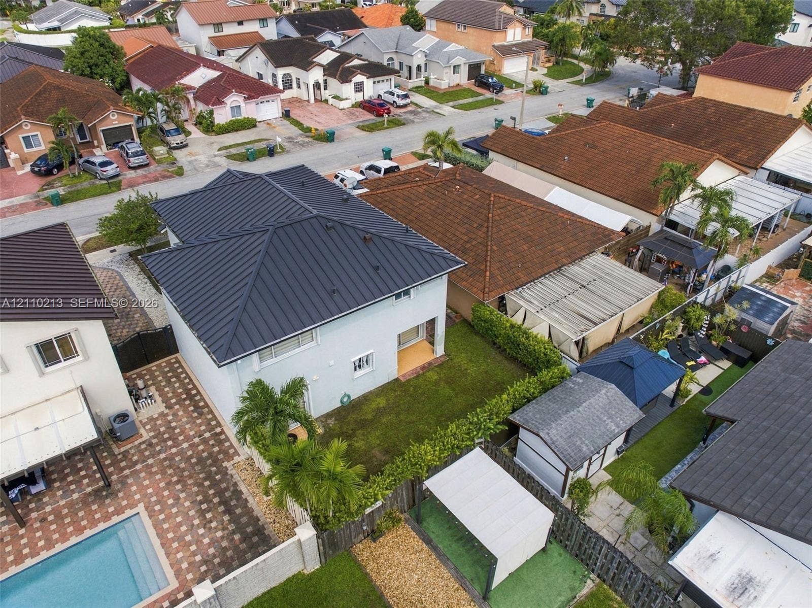 Two-story residence featuring a standing-seam metal roof, stucco exterior, rear yard with lawn, and perimeter hedging