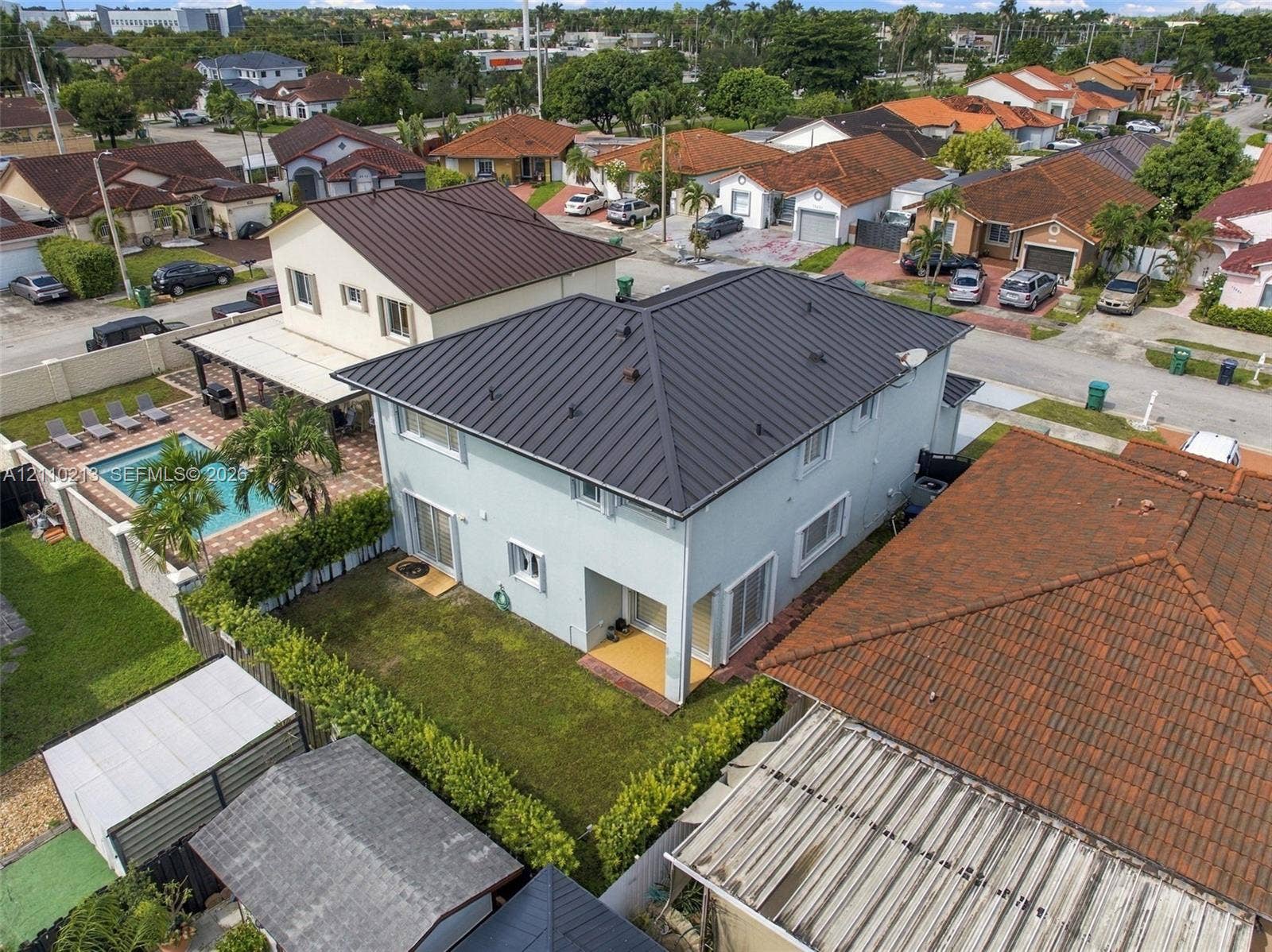 Two-story residence featuring a standing-seam metal roof, stucco exterior, private swimming pool, fenced backyard with mature hedges, and an attached covered patio
