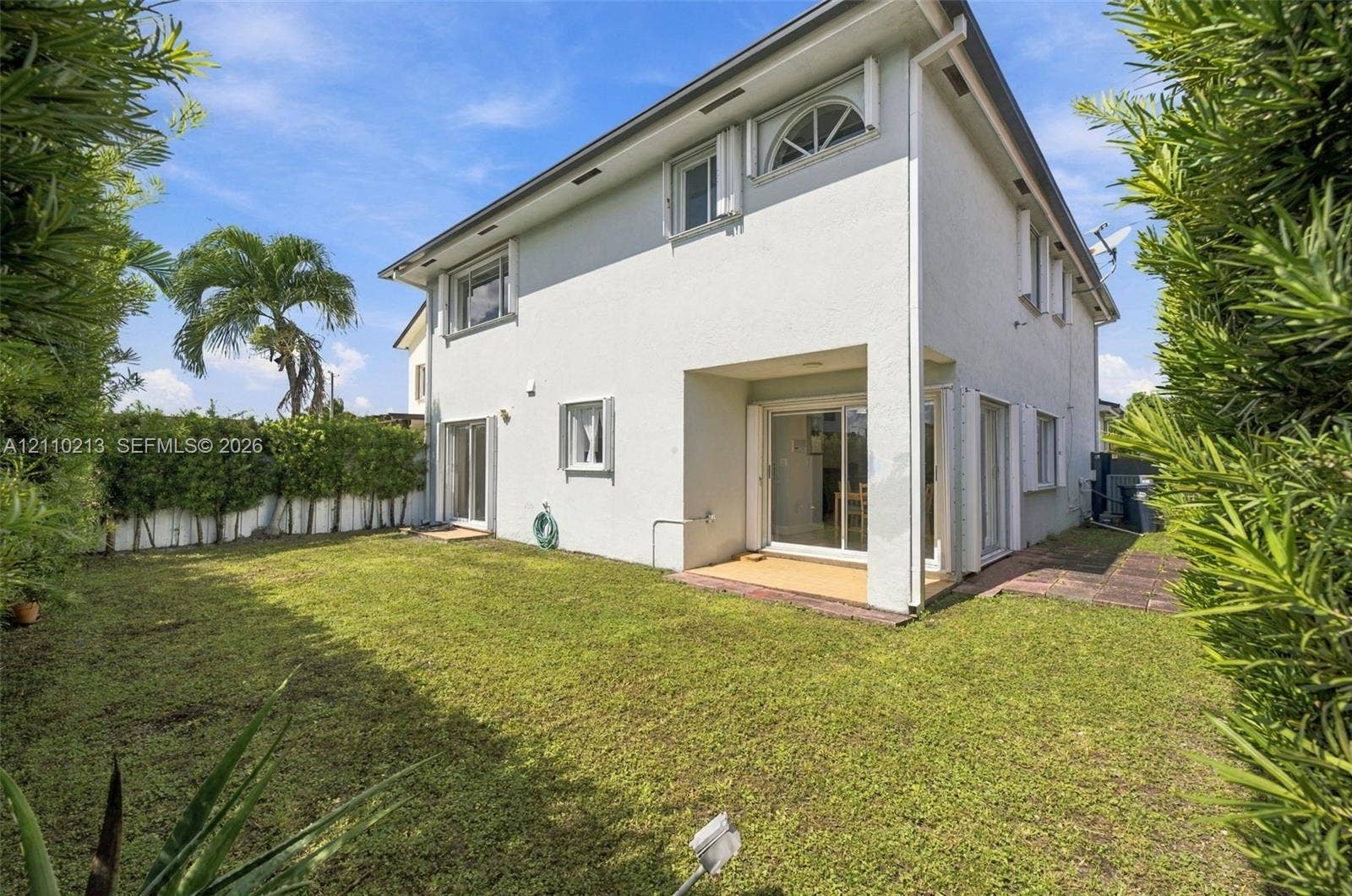 Two-story stucco exterior featuring sliding glass doors, a covered patio, and manicured perimeter hedges