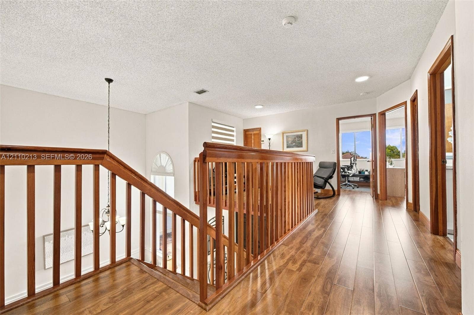 Landing area featuring wood-finish flooring, wood balustrade railing, recessed lighting, and a multi-tiered hanging light fixture