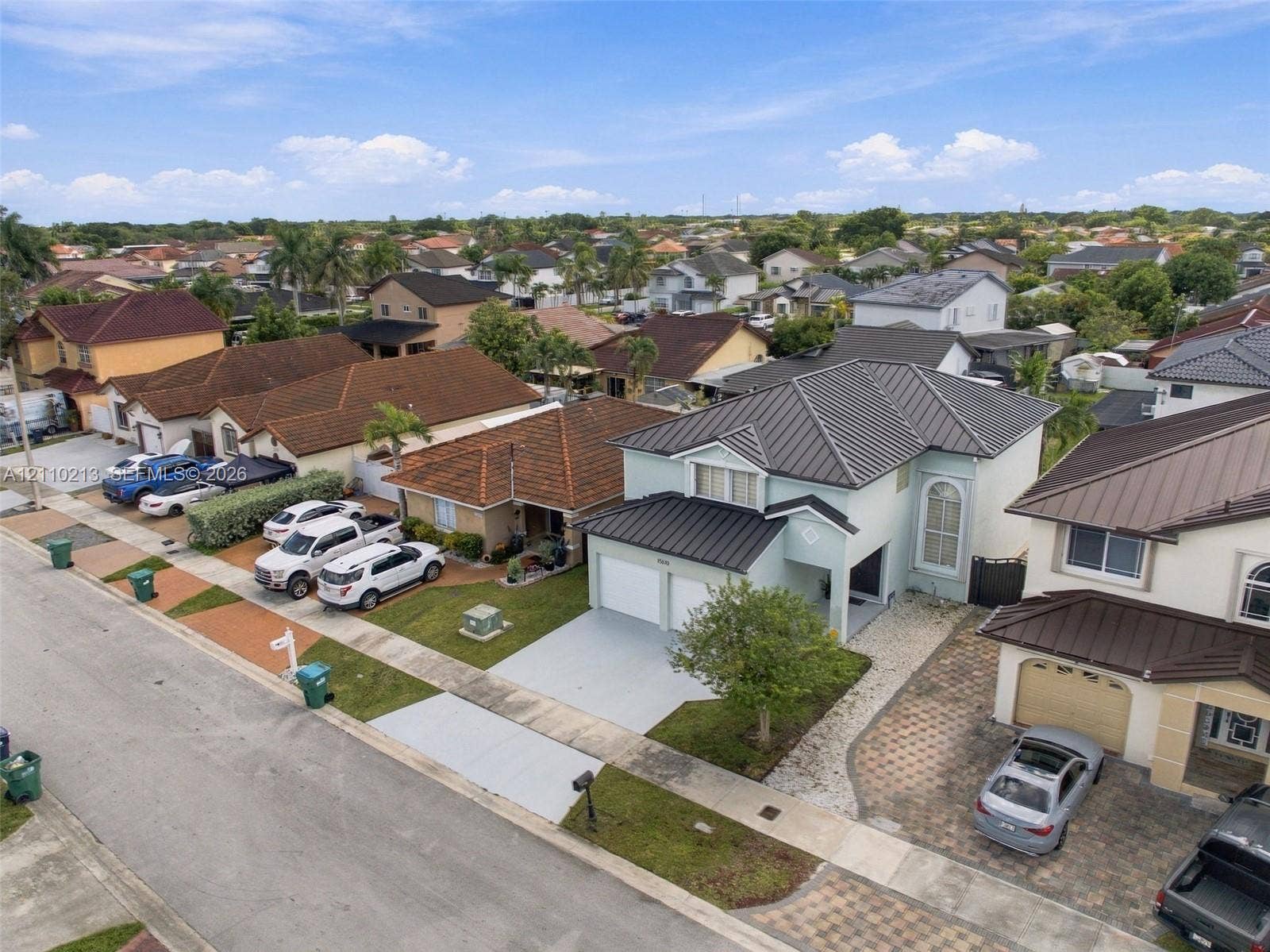 Two-story residence featuring a metal roof, light-colored stucco exterior, attached two-car garage, and a paver driveway