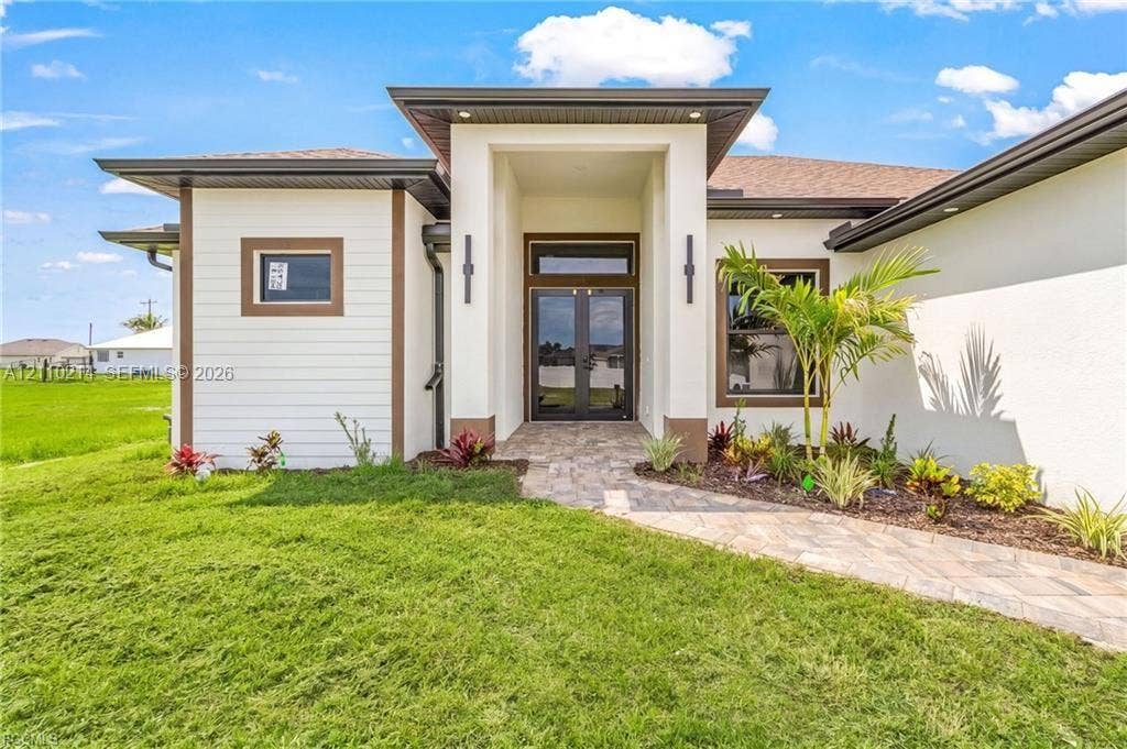 7 SW 19th Place, Cape Coral, FL 33991 Contemporary exterior featuring a stone-paved entryway, horizontal lap siding, a glass-paneled double door, and architectural lighting fixtures