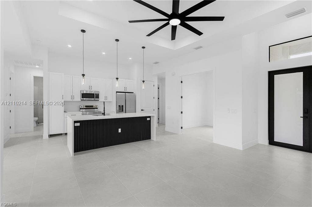 7 SW 19th Place, Cape Coral, FL 33991 Kitchen featuring a center island with slat detailing and a solid-surface countertop, white cabinetry, integrated stainless steel appliances, large-format tile flooring, and a coffered ceiling with a multi-blade ceiling fan