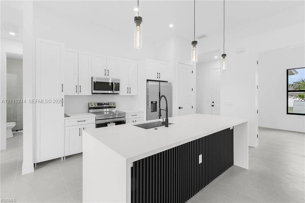 7 SW 19th Place, Cape Coral, FL 33991 Kitchen featuring white cabinetry, quartz countertops, a black slatted-detail island with an undermount sink, matte black faucet, and three glass pendant lights