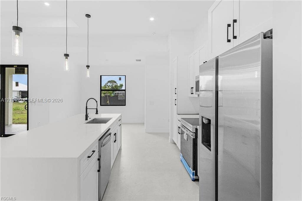 7 SW 19th Place, Cape Coral, FL 33991 Kitchen featuring a central island with a solid surface countertop, stainless steel appliances, white cabinetry with matte black hardware, and pendant lighting