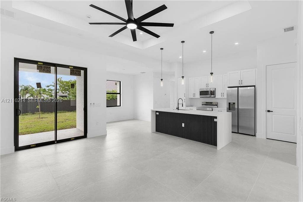 7 SW 19th Place, Cape Coral, FL 33991 Open-concept area featuring a coffered ceiling with a black multi-blade ceiling fan, large-format tile flooring, a kitchen island with a slatted base and quartz-finish countertop, stainless steel appliances, and sliding glass doors