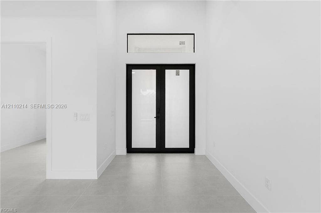 7 SW 19th Place, Cape Coral, FL 33991 Double front doors featuring matte black frames with glass panel inserts, complemented by a rectangular transom window and large-format tile flooring