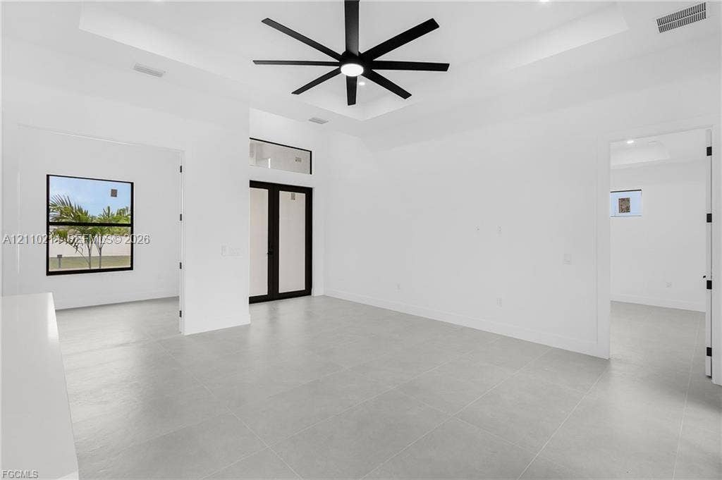 7 SW 19th Place, Cape Coral, FL 33991 Tray ceiling, large-format tile flooring, matte black multi-blade ceiling fan, and black-framed glass entry doors with transom window